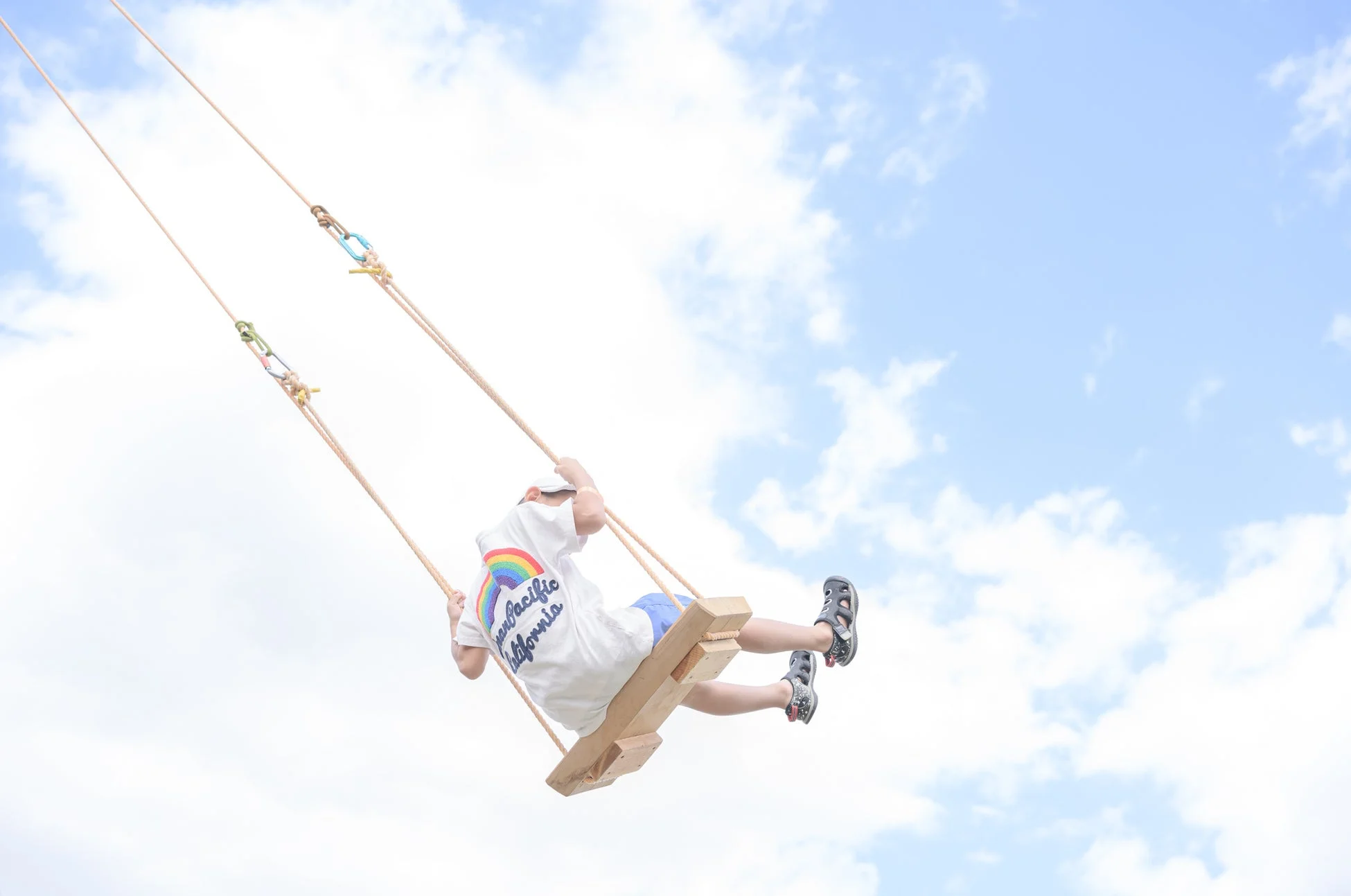 青い空と白い雲を背景に、子供がぶらんこに乗り高く漕いでいる様子