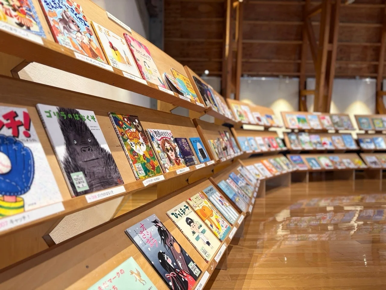 木製の棚に多数の絵本や児童書が弧状に陳列されている図書館または書店の一角