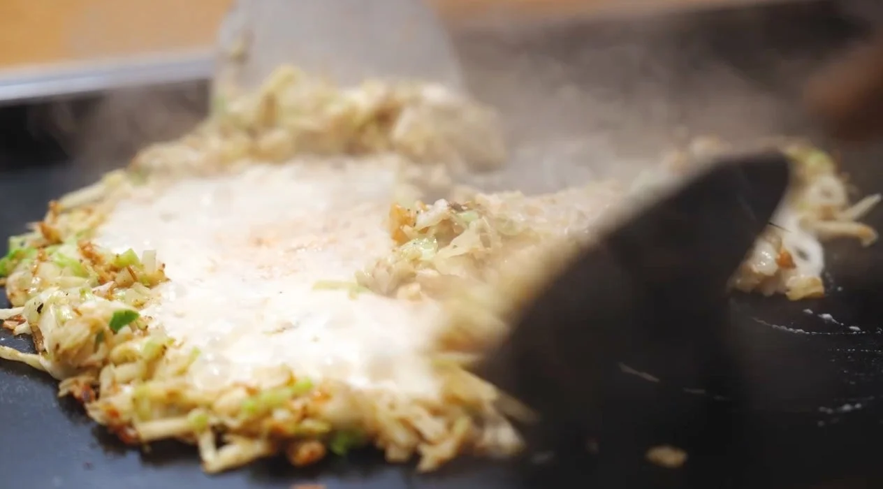 鉄板で調理されるお好み焼きのような料理