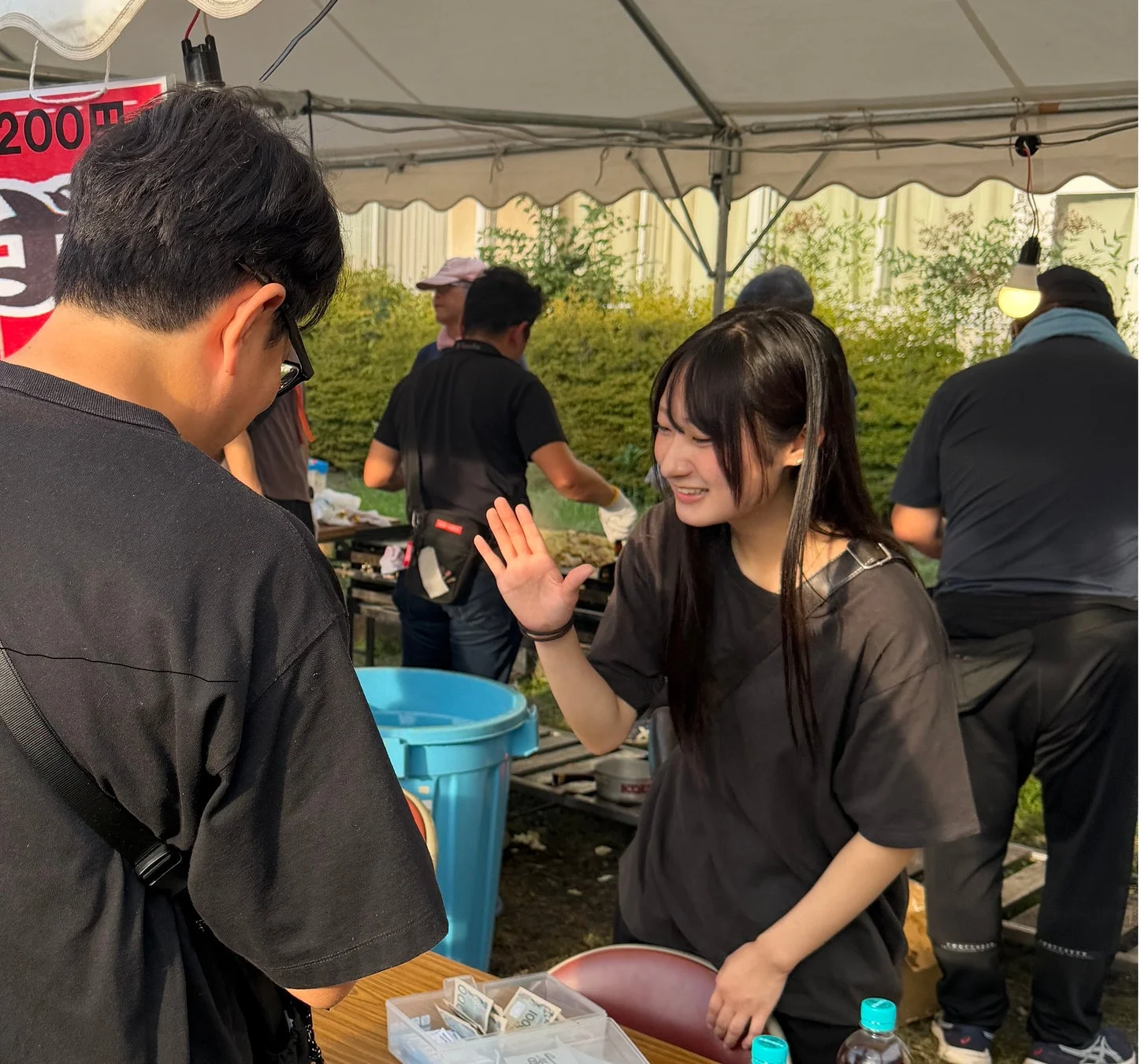 屋外のイベント会場で、若い女性が笑顔で客と会話している様子